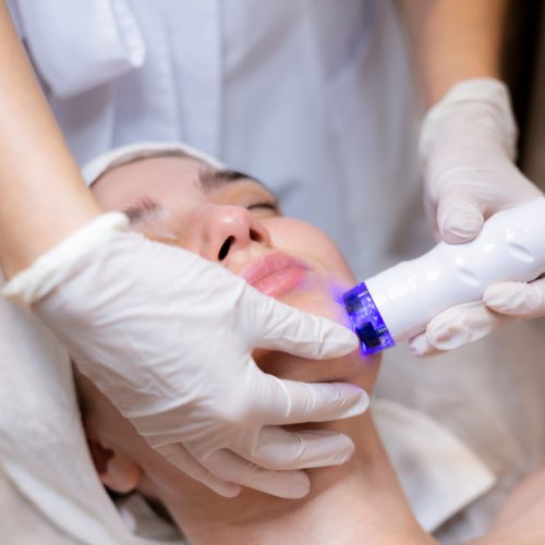 A young beautiful girl lies on the beautician's table and receives procedures with a professional apparatus for skin rejuvenation and moisturizing